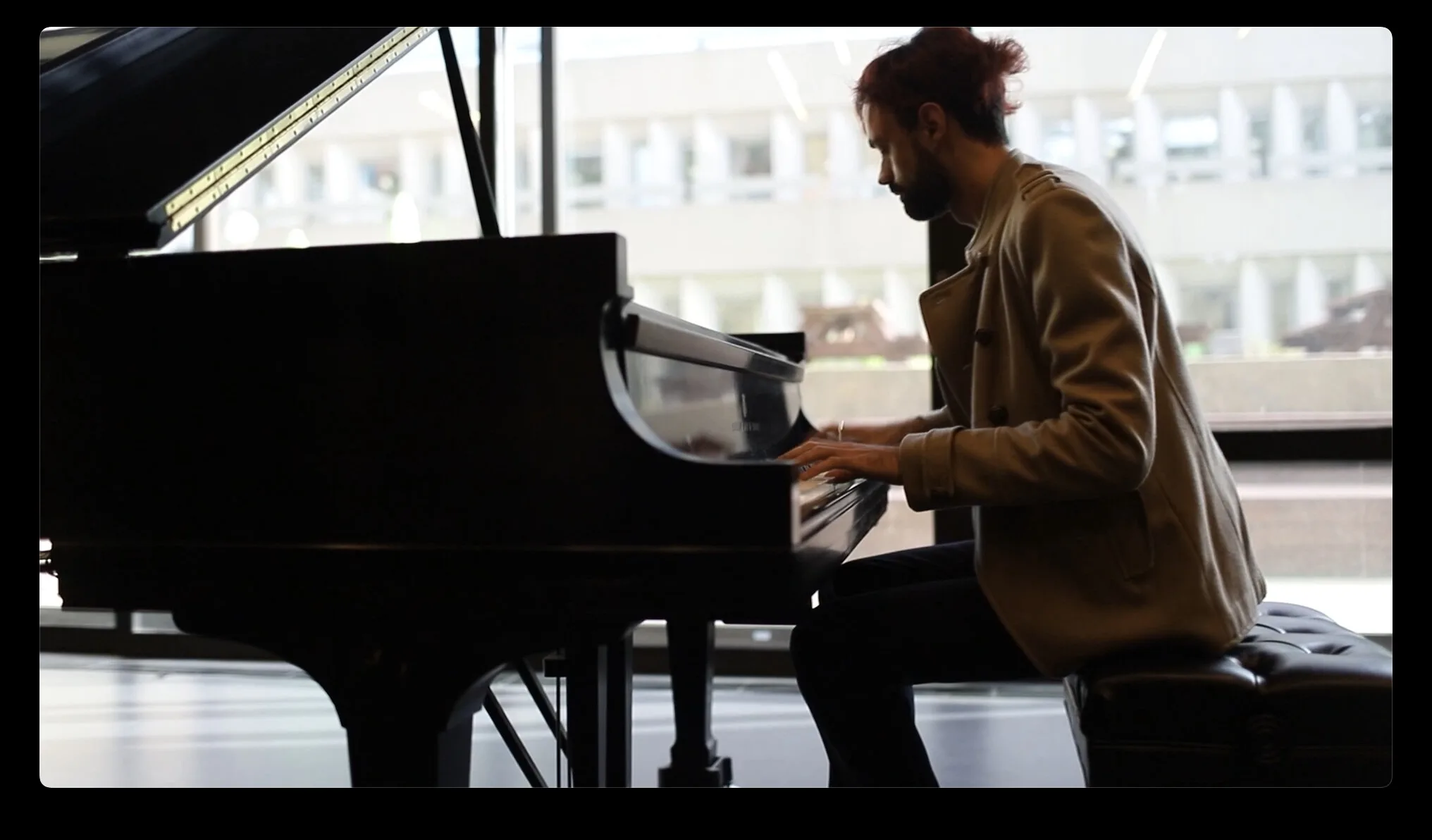 Mircea au piano à queue devant une grande fenêtre, en pleine performance.