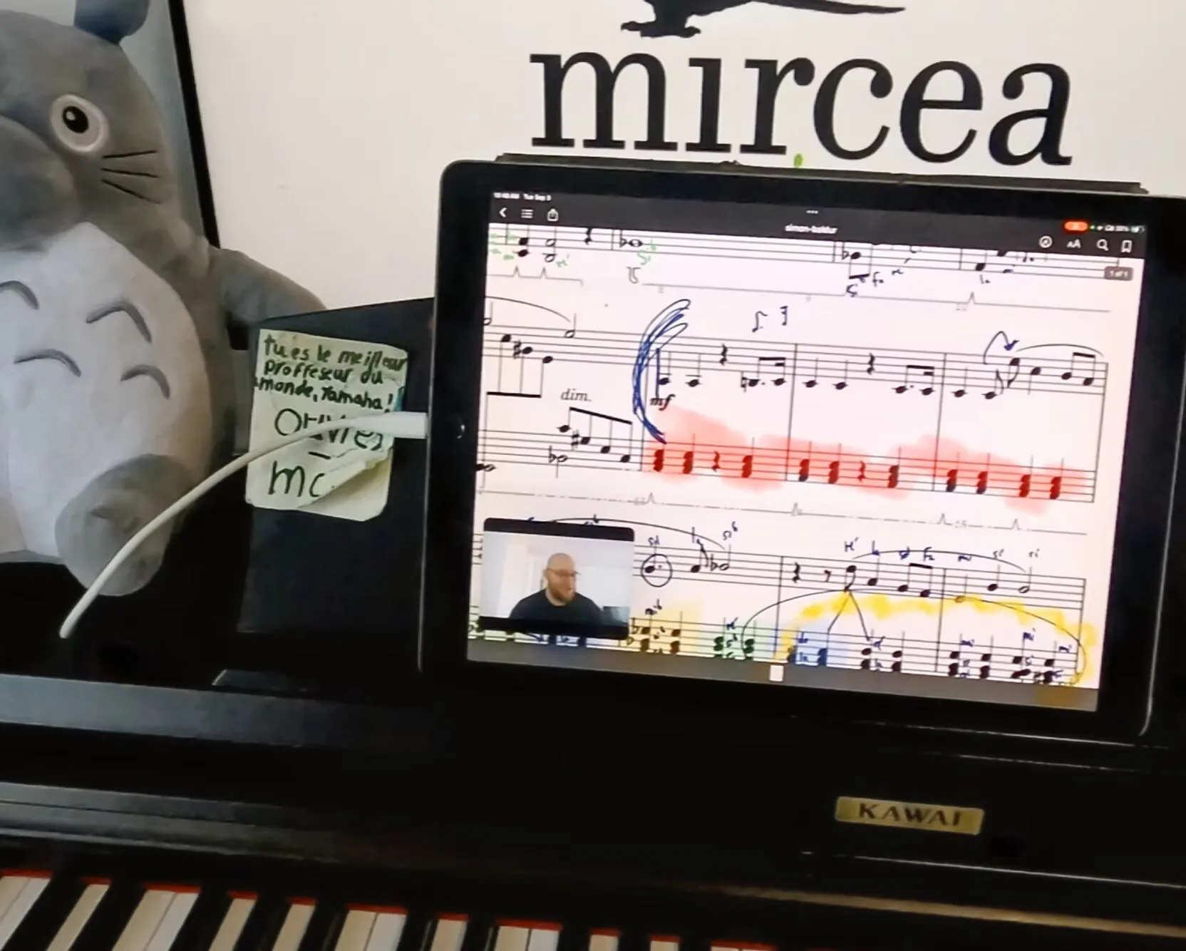 Une partition annotée sur tablette pendant une leçon, avec un mot d'un élève sur le piano.